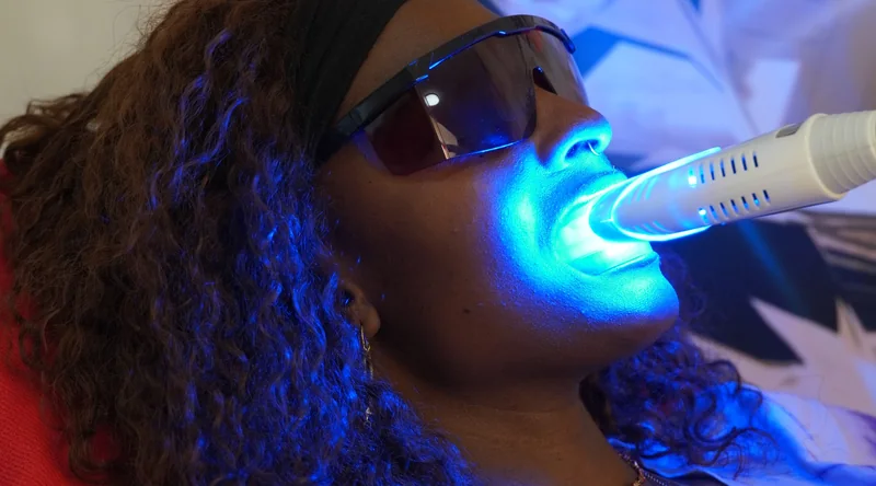 Die Aufhellungslampe leuchtet auf die Zähne, die Kundin trägt eine Schutzbrille
